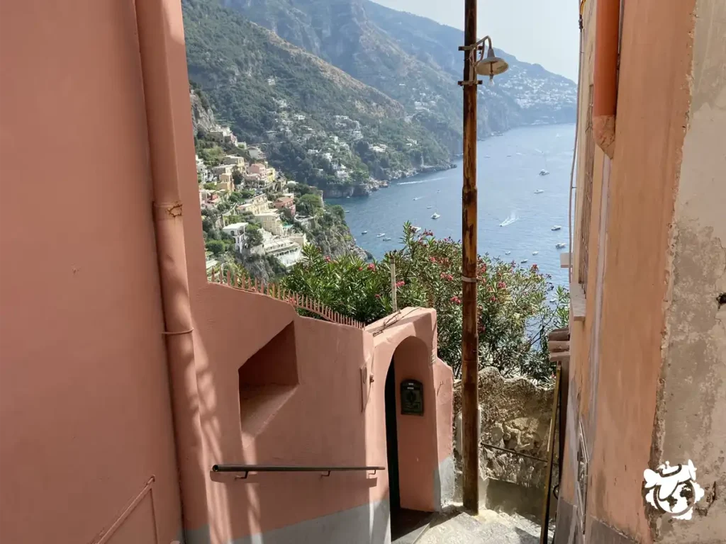 Una calle de Positano, en la Costa Amalfitana con murallas rosadas y la visa del mar